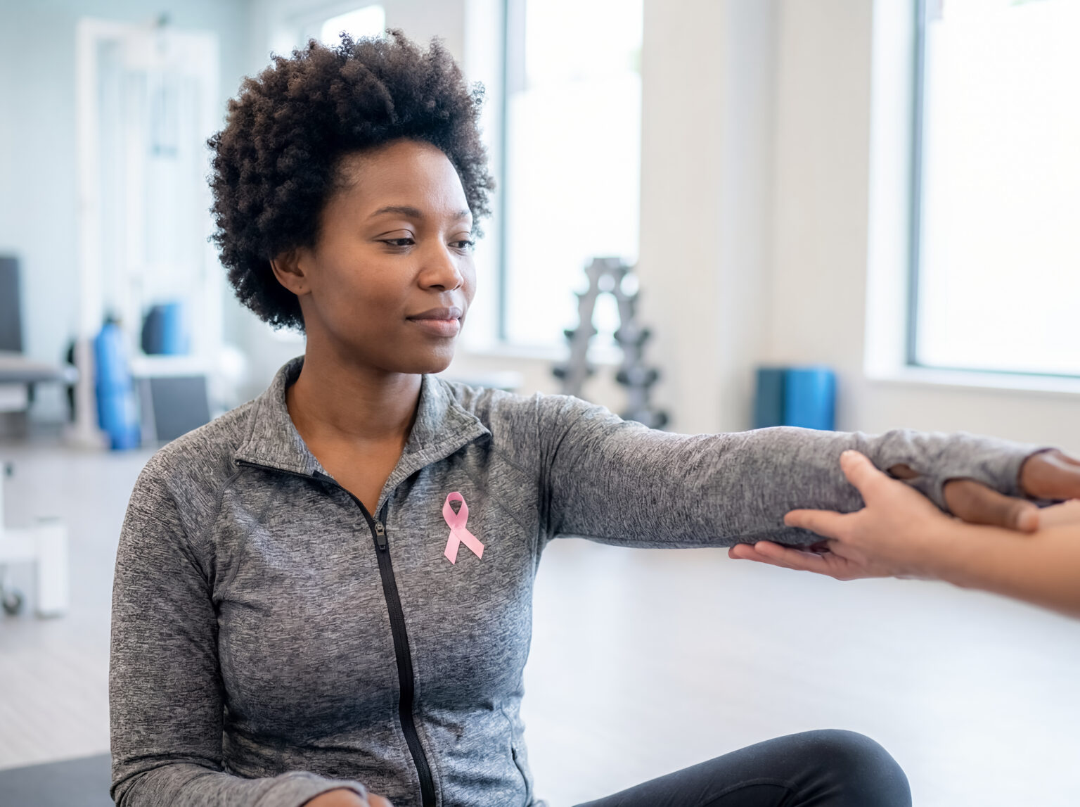 Breast cancer survivor woman receiving physical therapy arm rehabilitation pink ribbon awareness black female with therapist hand support recovery treatment care medical assistance and healing theme